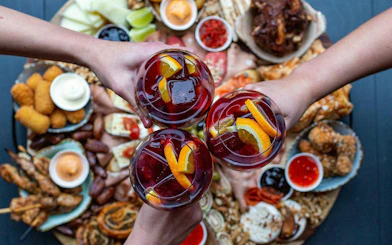 Hands holding glasses of sangria over a spread of tapas during Valencia cooking class.