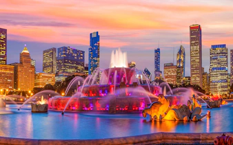 Buckingham Fountain illuminated at night with Chicago skyline in the background.