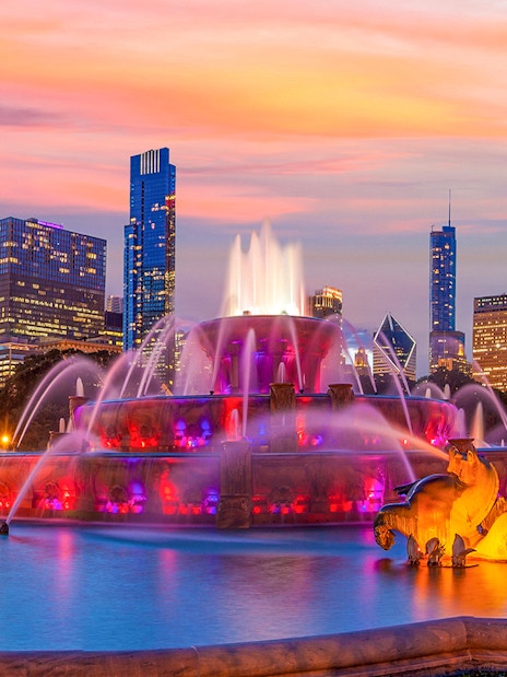 Buckingham Fountain illuminated at night with Chicago skyline in the background.