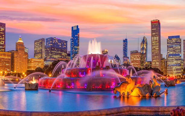 Buckingham Fountain illuminated at night with Chicago skyline in the background.