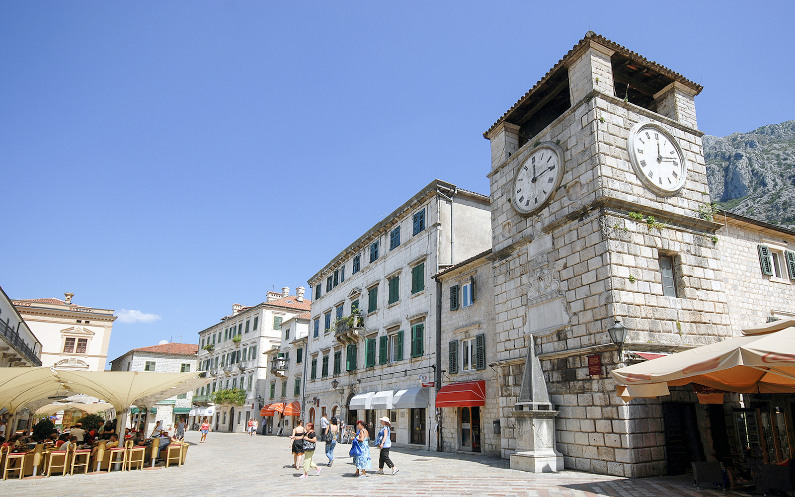 Clock tower in Kotor, Montenegro with nearby shops and people walking.