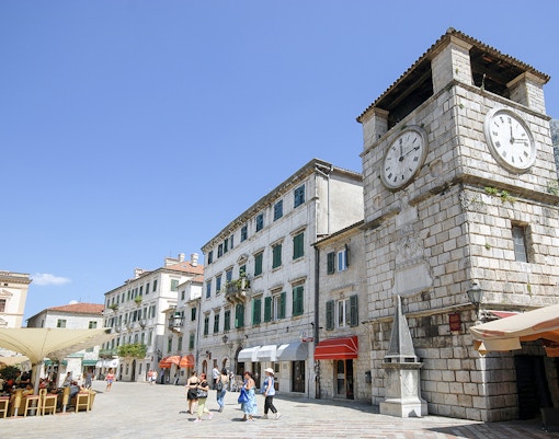 Clock tower in Kotor, Montenegro with nearby shops and people walking.