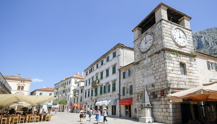 Clock tower in Kotor, Montenegro with nearby shops and people walking.