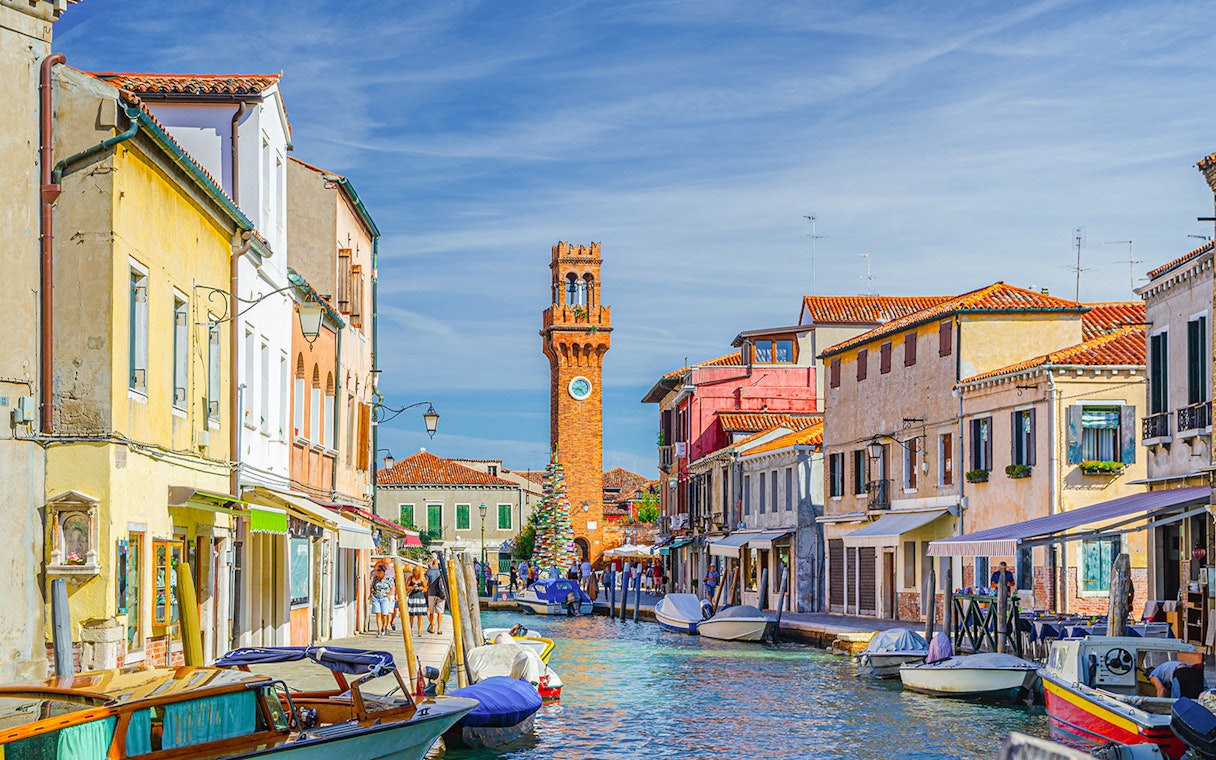Murano canal with Torre dell'Orologio clock tower and colorful buildings.