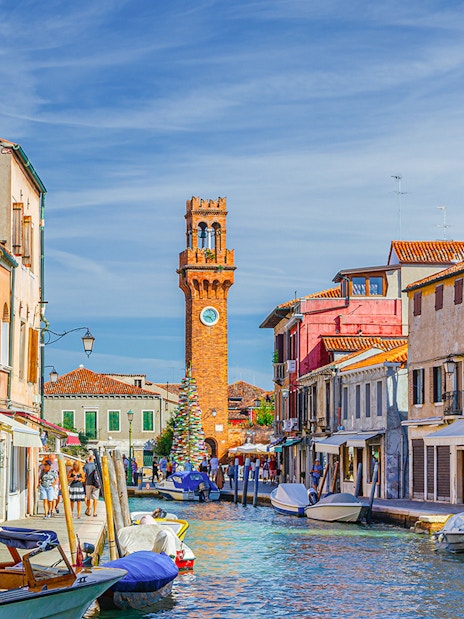 Murano canal with Torre dell'Orologio clock tower and colorful buildings.