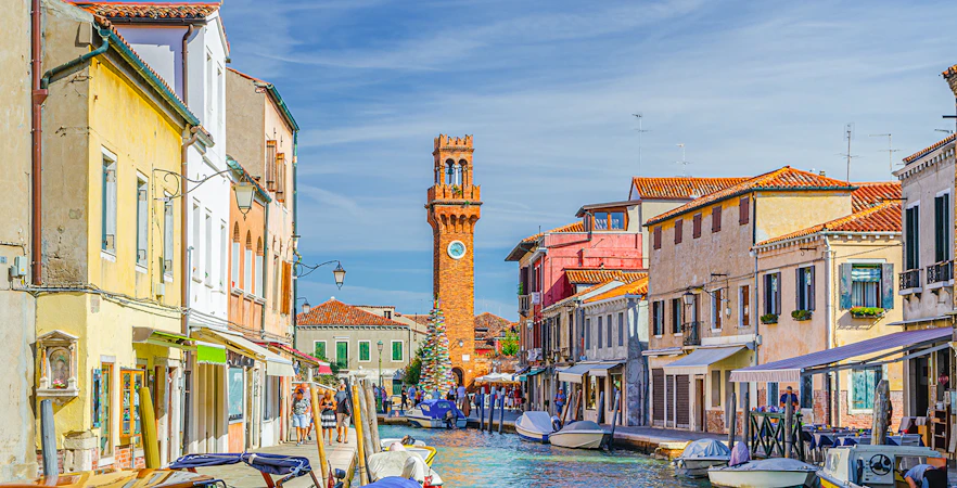 Murano canal with Torre dell'Orologio clock tower and colorful buildings.