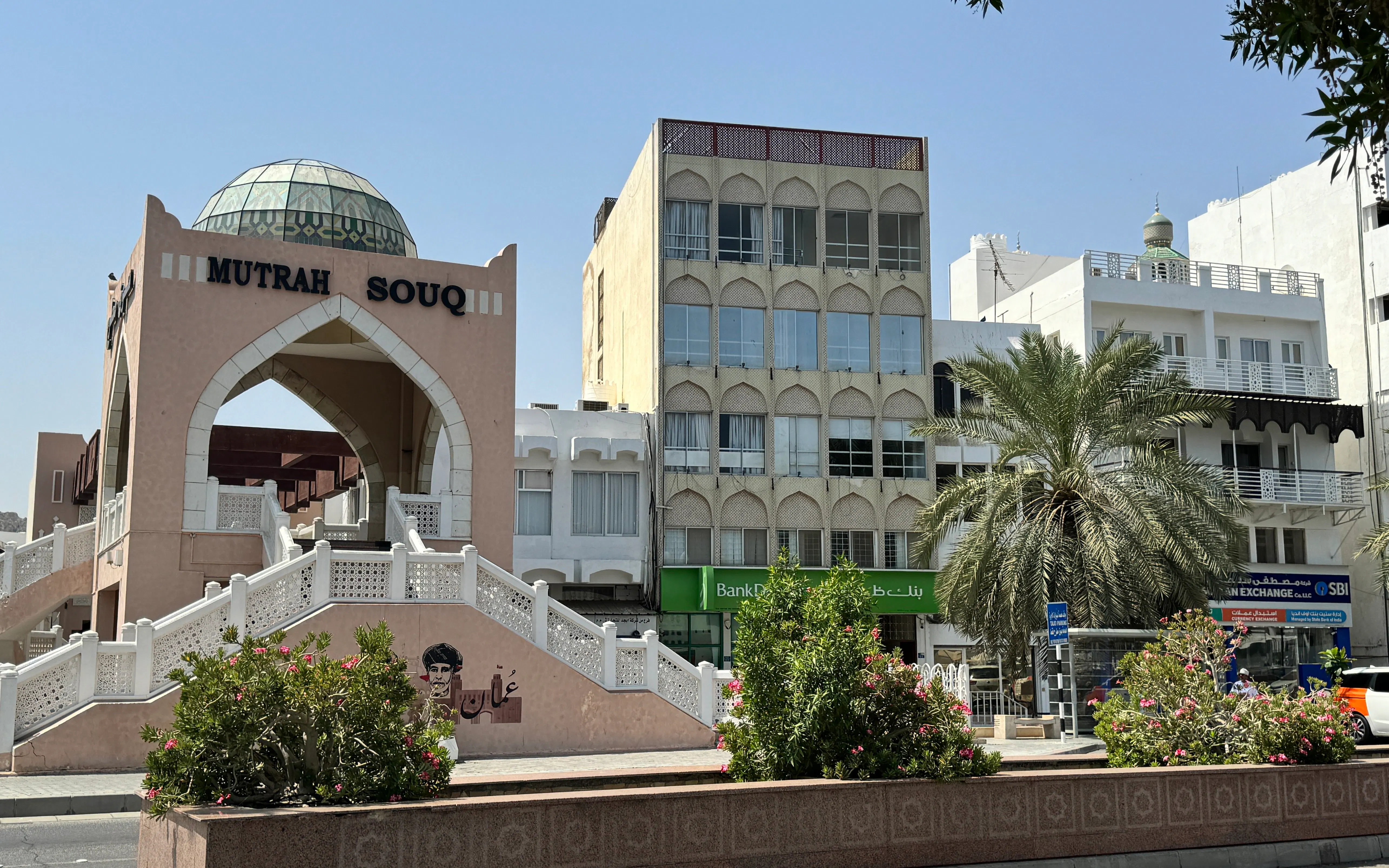 Entrance of Mutrah Souq in Muscat with surrounding buildings and palm tree.