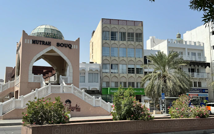 Entrance of Mutrah Souq in Muscat with surrounding buildings and palm tree.