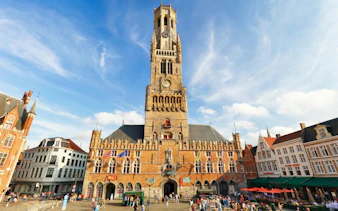 Belfry Tower in Bruges, Belgium, with tourists in the historical square.
