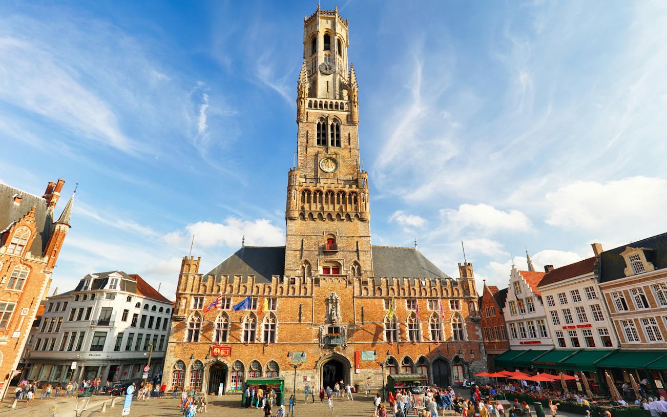 Belfry Tower in Bruges, Belgium, with tourists in the historical square.