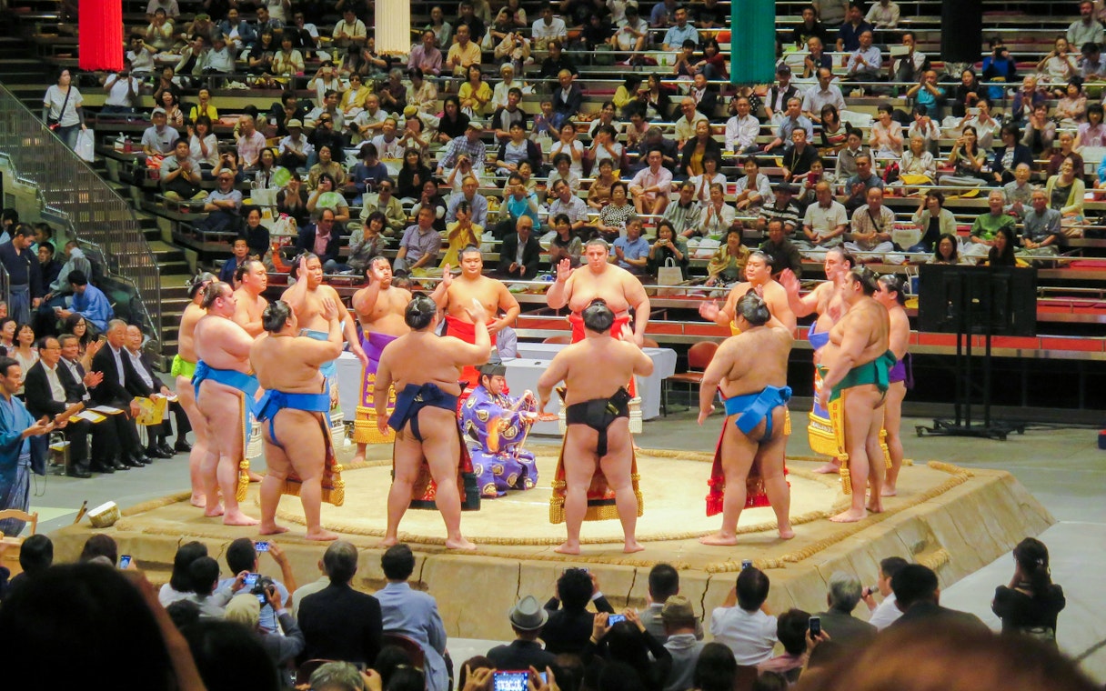 Sumo wrestlers in a Tokyo ring with a large crowd watching.