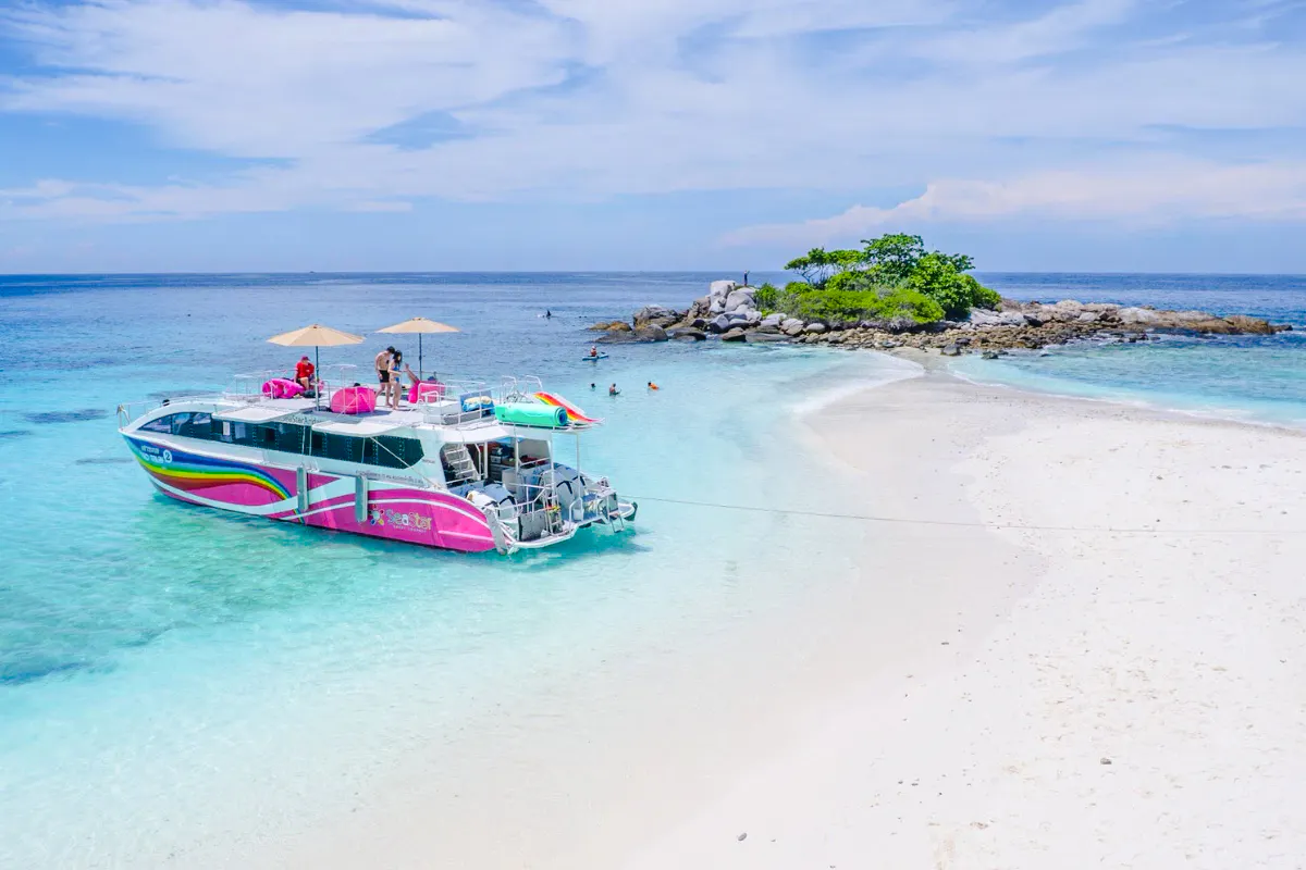 Speed catamaran near Racha Noi island with tourists enjoying the beach and clear waters.