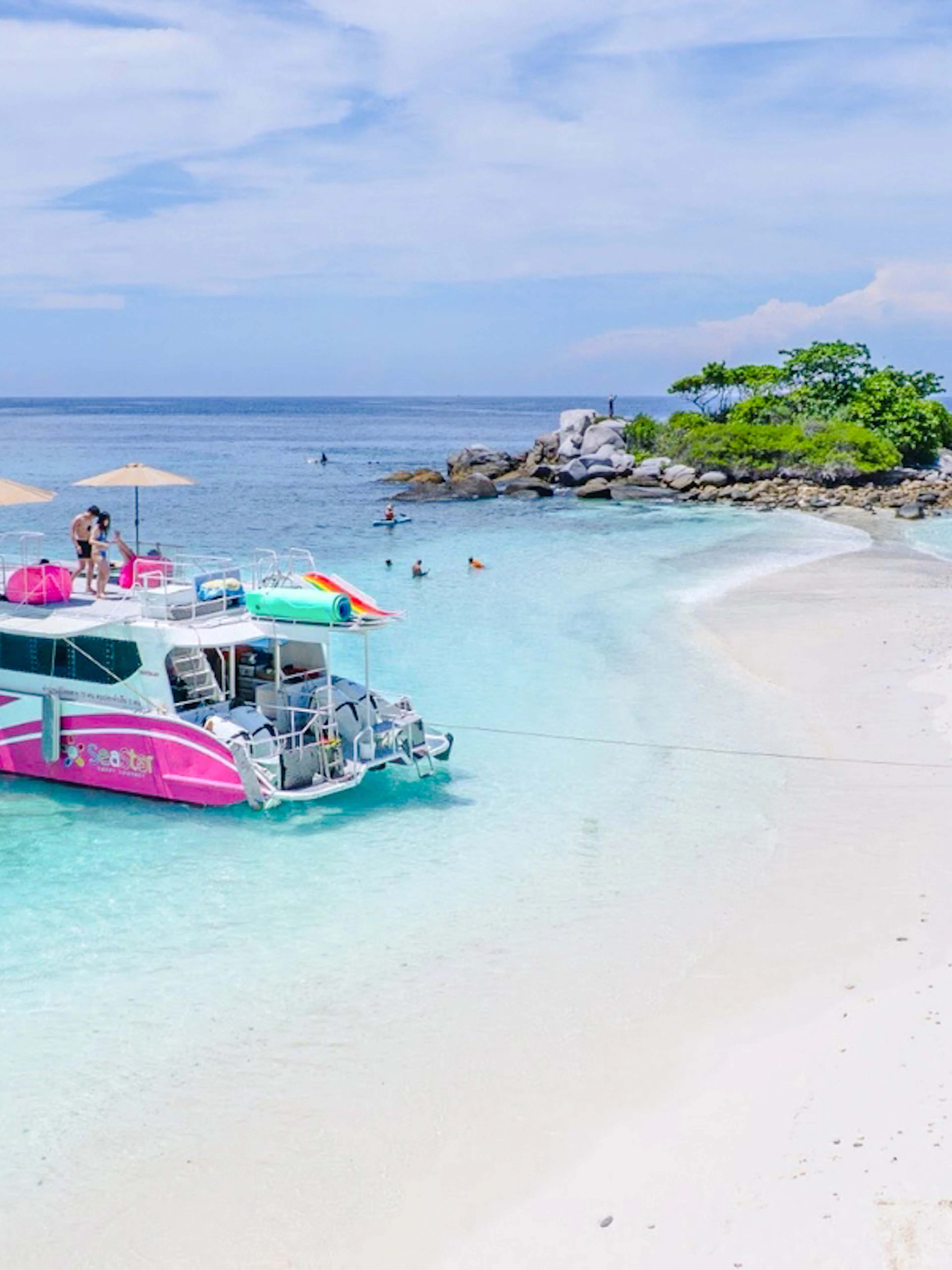 Speed catamaran near Racha Noi island with tourists enjoying the beach and clear waters.