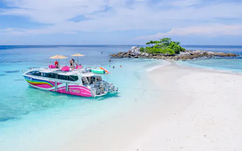 Speed catamaran near Racha Noi island with tourists enjoying the beach and clear waters.