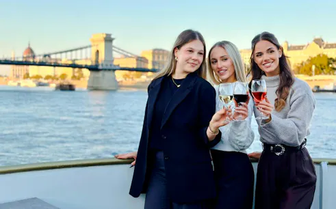 Guests toasting with wine on Budapest river cruise with Chain Bridge in background.