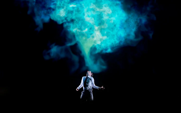Person standing under blue smoke in a dramatic scene from Stranger Things: The First Shadow.