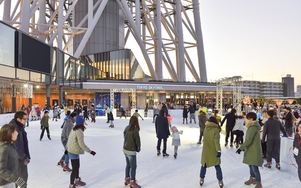 People ice skating at the base of Tokyo Skytree in the evening.