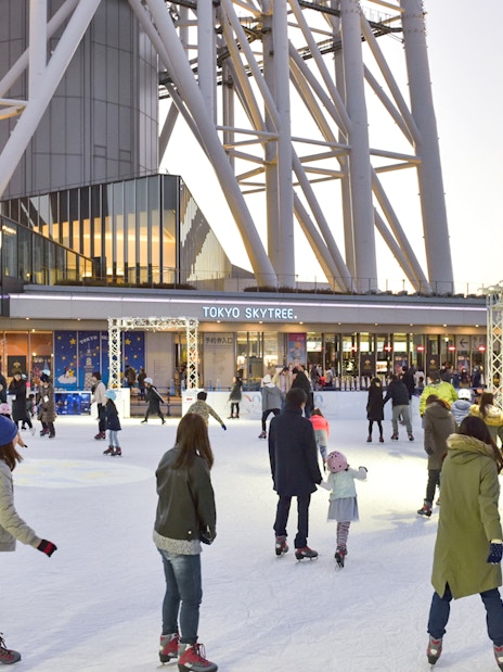 People ice skating at the base of Tokyo Skytree in the evening.
