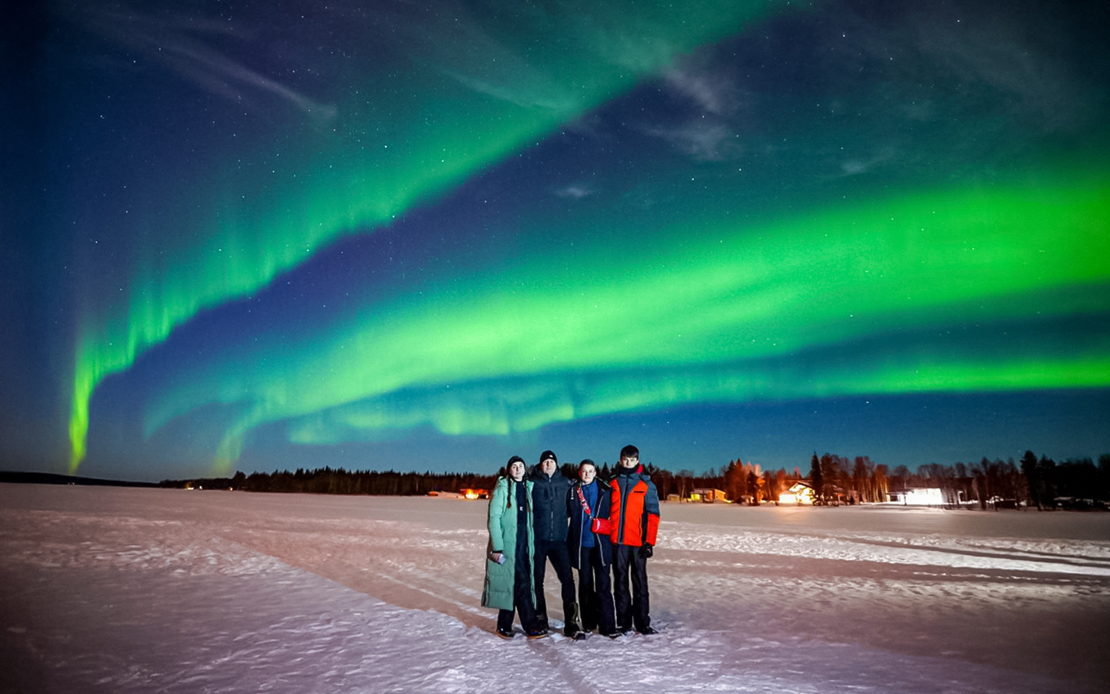 Guests on Northern Lights Chase tour under vibrant aurora in snowy landscape.
