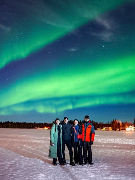 Guests on Northern Lights Chase tour under vibrant aurora in snowy landscape.