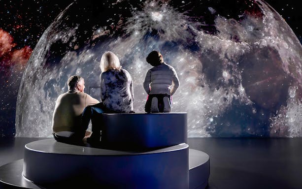 Visitors viewing a large moon projection at a space-themed exhibit.