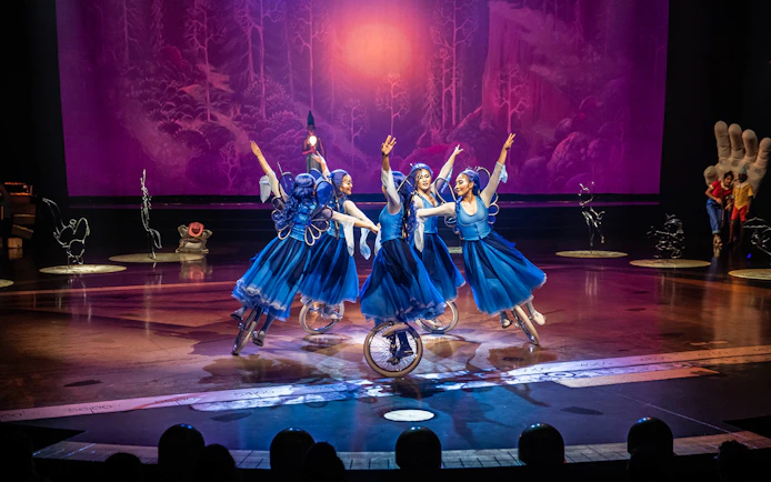 Performers in blue costumes ride unicycles in a theatrical show, "Drawn to Life.