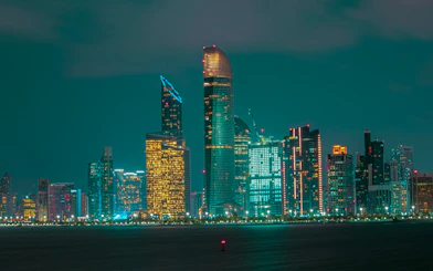 Abu Dhabi skyline at night with illuminated skyscrapers, viewed from the water.