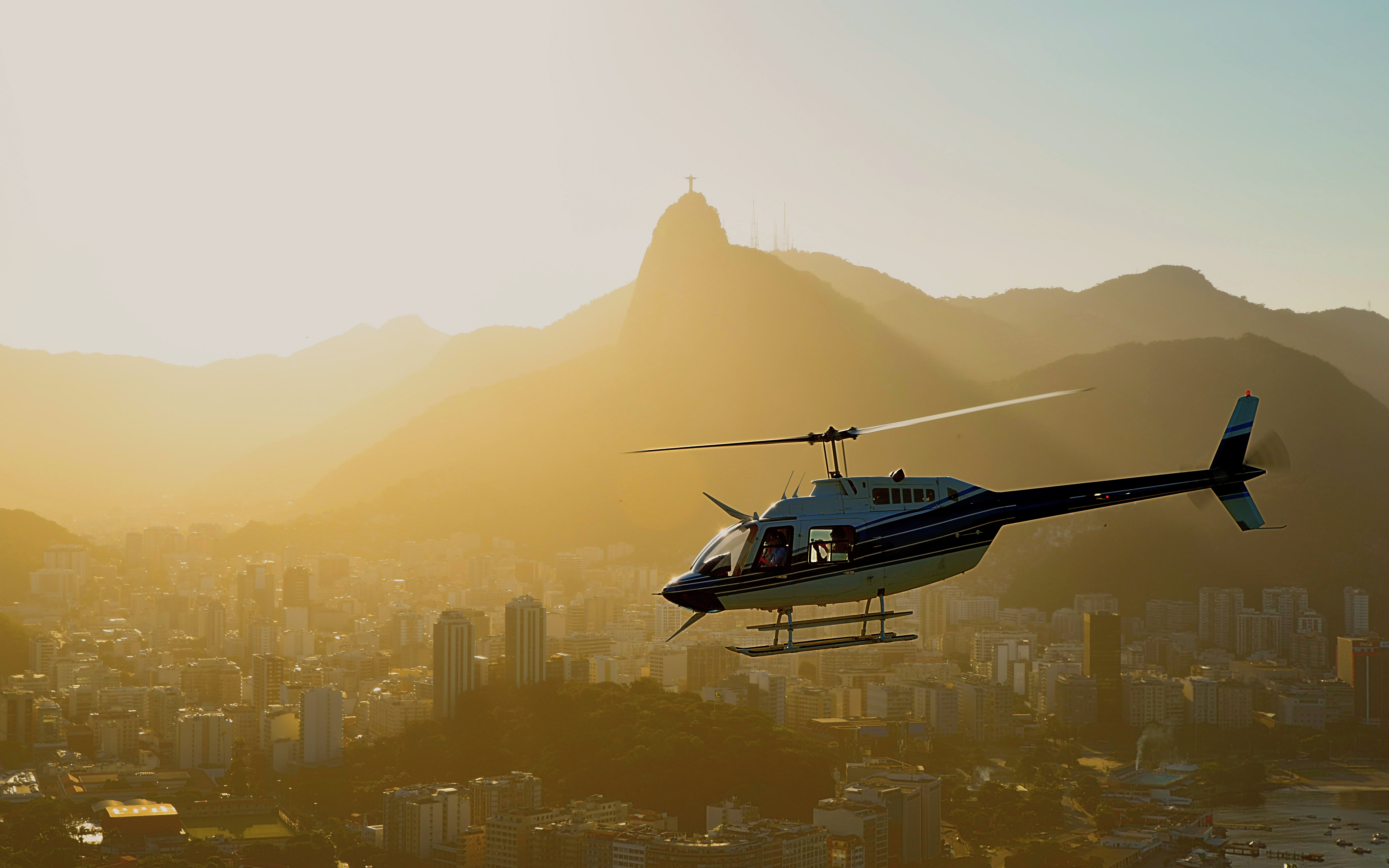 Helicopter taking off over Rio de Janeiro at sunset with Sugarloaf Mountain in view.
