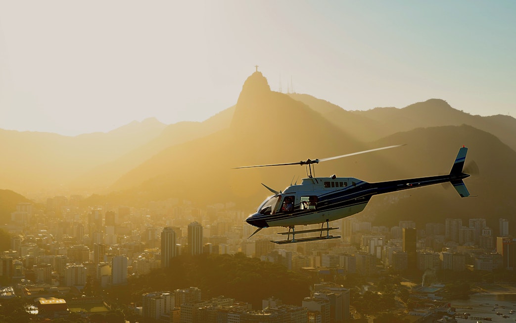 Helicopter taking off over Rio de Janeiro at sunset with Sugarloaf Mountain in view.