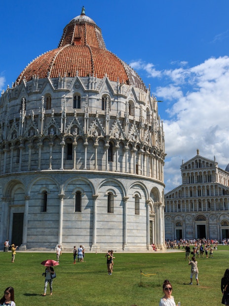 Pisa Baptistery with tourists on the lawn, Pisa, Italy.
