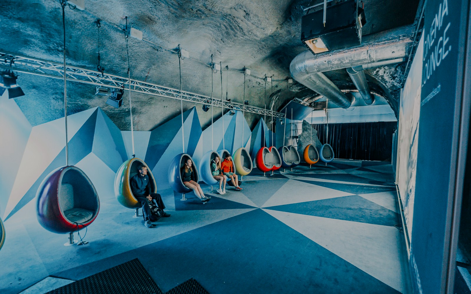 People seated in modern hanging chairs in a cinema room.