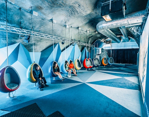 People seated in modern hanging chairs in a cinema room.