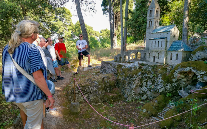 Tour group exploring a miniature stone church model in a forest near Zadar.