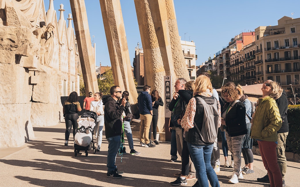 Tour guide with tourists at Sagrada Familia entrance on a sunny day in Barcelona.