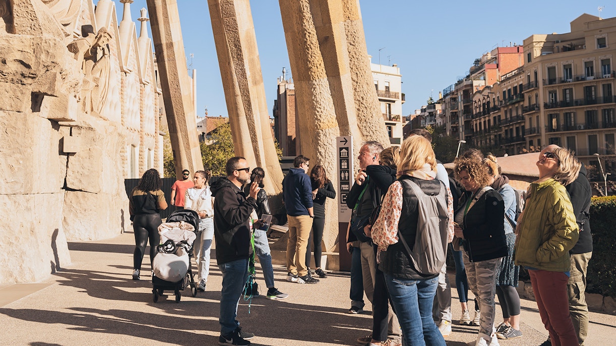 Tour guide with tourists at Sagrada Familia entrance on a sunny day in Barcelona.