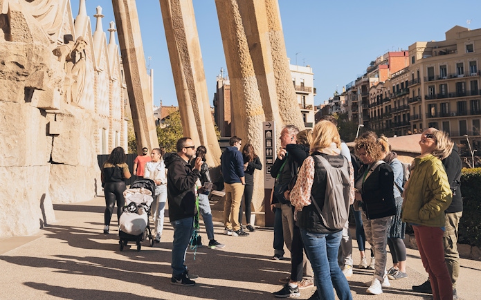 Tour guide with tourists at Sagrada Familia entrance on a sunny day in Barcelona.