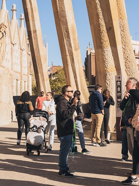 Tour guide with tourists at Sagrada Familia entrance on a sunny day in Barcelona.