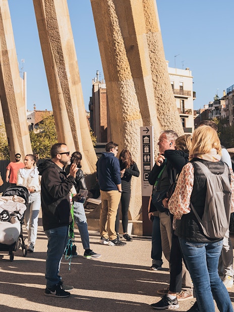 Tour guide with tourists at Sagrada Familia entrance on a sunny day in Barcelona.