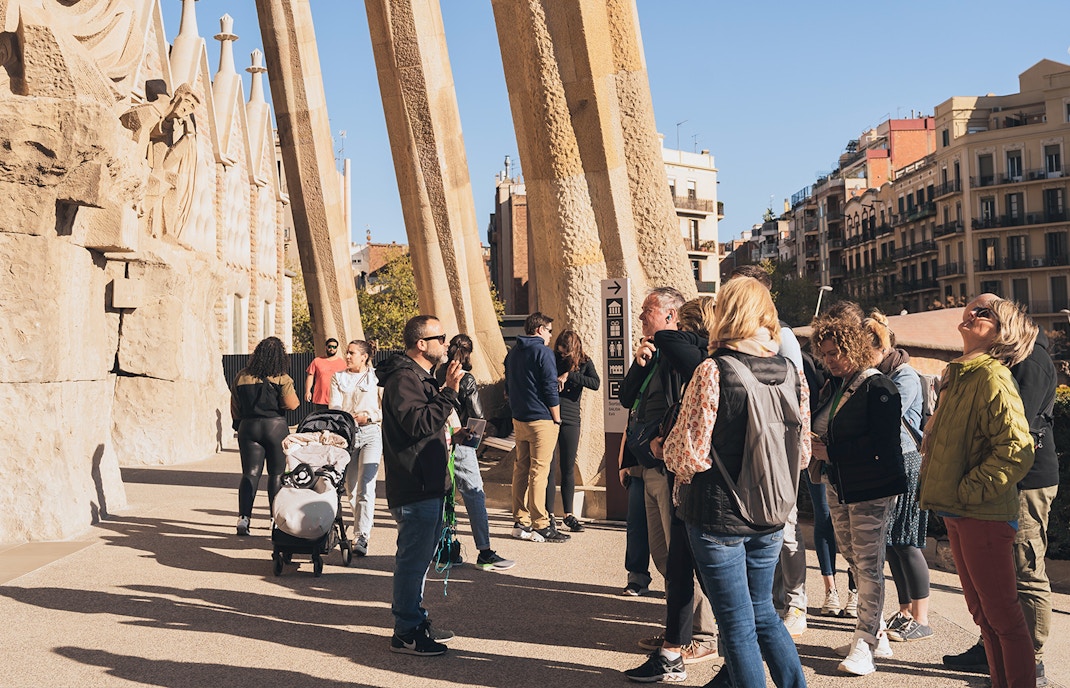 Tour guide with tourists at Sagrada Familia entrance on a sunny day in Barcelona.