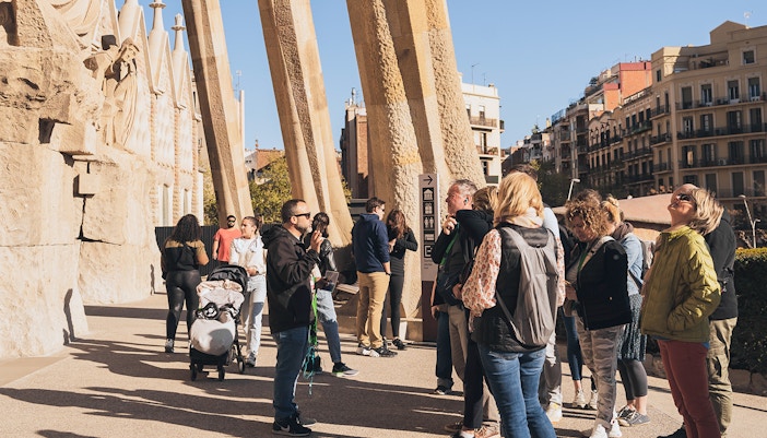 Tour guide with tourists at Sagrada Familia entrance on a sunny day in Barcelona.
