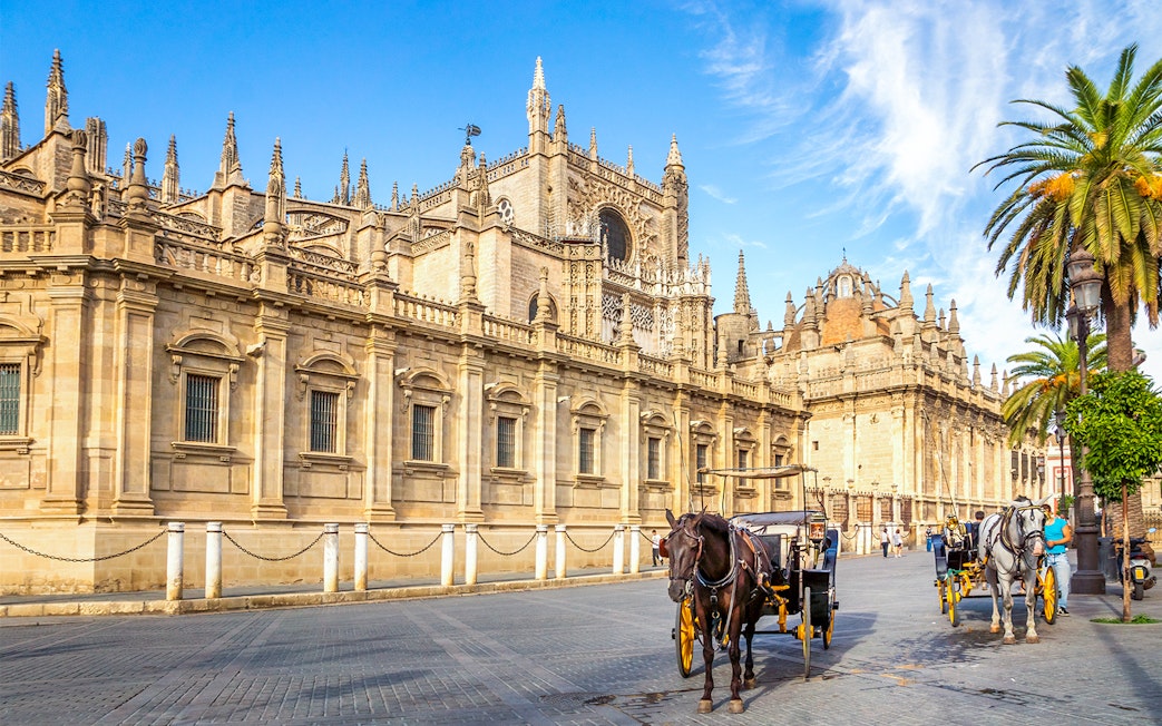 Seville Cathedral exterior with horse-drawn carriages on the street.