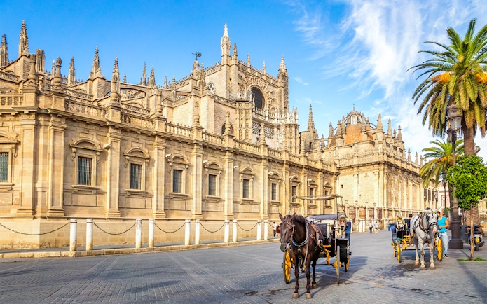 Seville Cathedral exterior with horse-drawn carriages on the street.