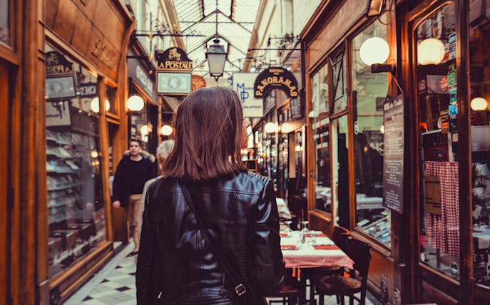 Person walking through a covered passage in Paris with shops and cafes.
