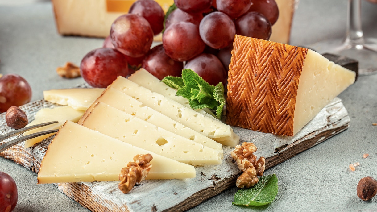 Sliced Manchego cheese with grapes and walnuts on a rustic board.