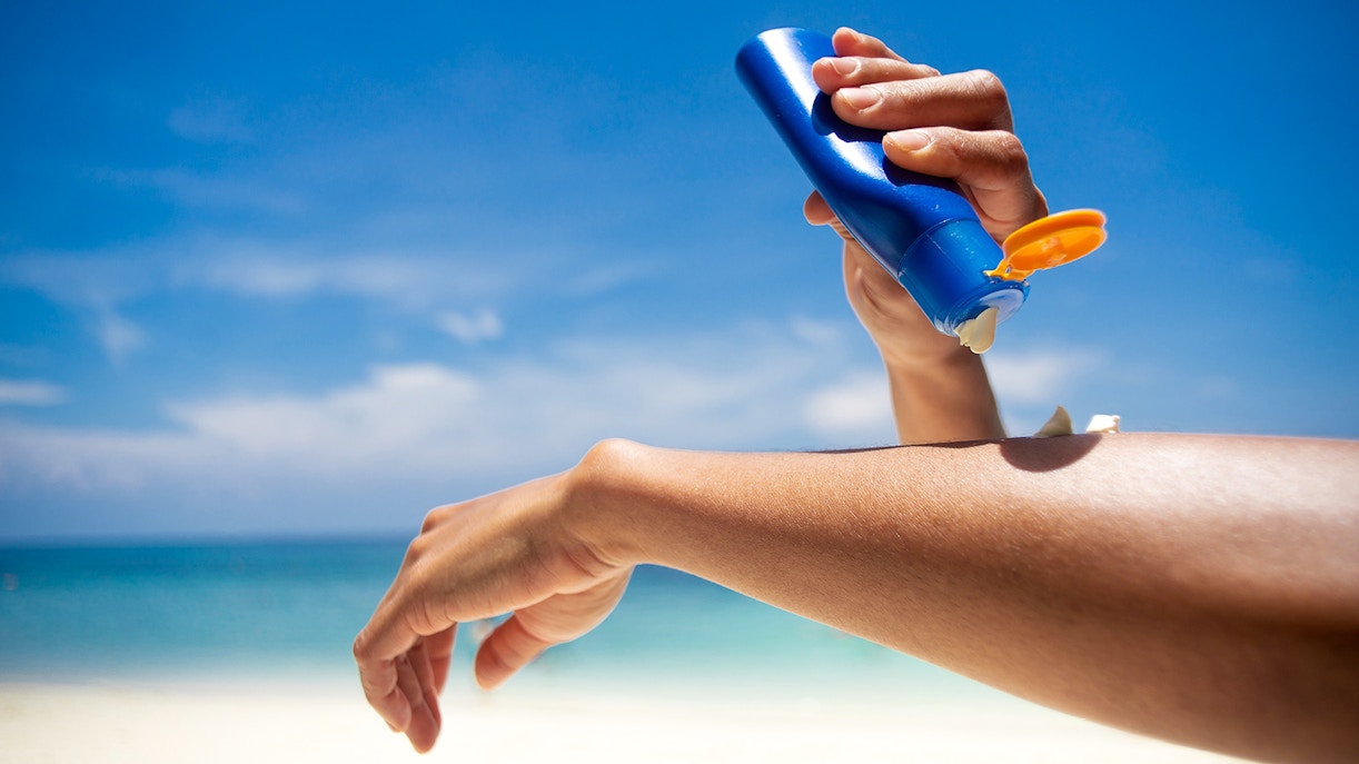 Woman applying sunscreen on arm at a sunny beach.