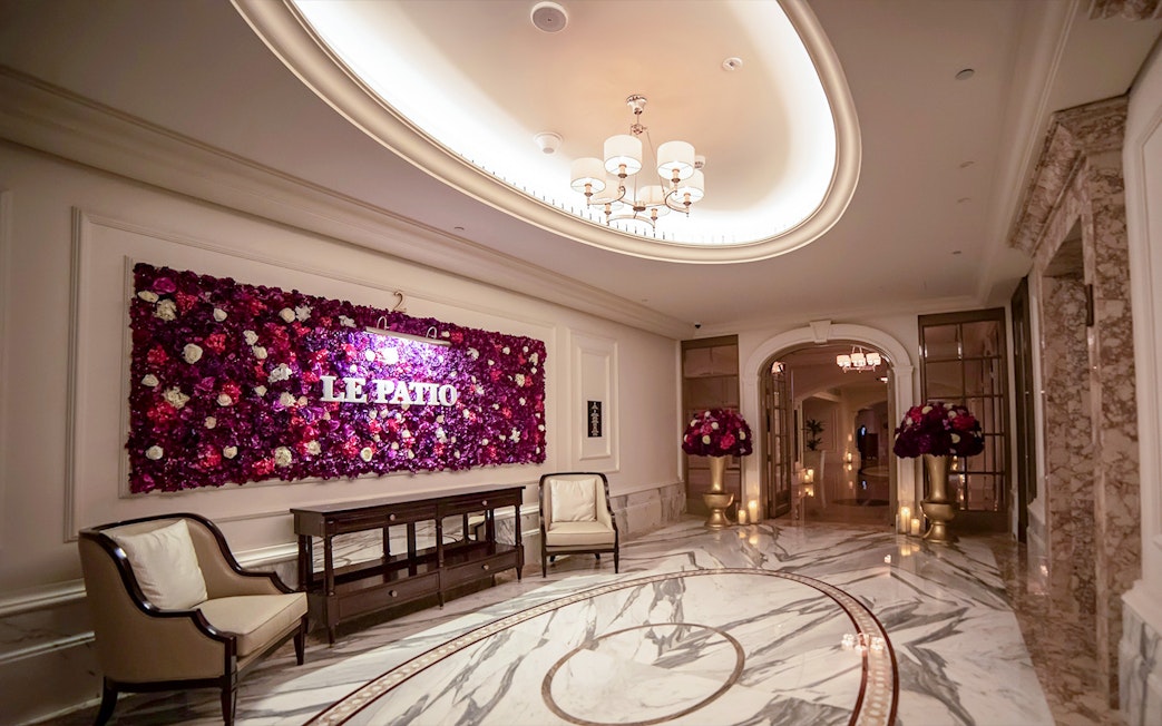 Le Patio Restaurant entrance with floral wall decor, elegant seating, and marble flooring.