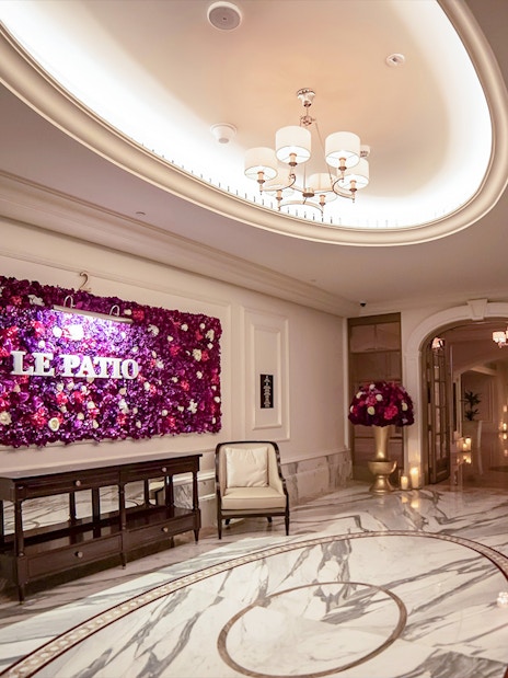 Le Patio Restaurant entrance with floral wall decor, elegant seating, and marble flooring.