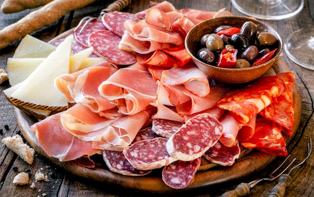 Charcuterie board with assorted meats, cheeses, and olives at a West End London restaurant.