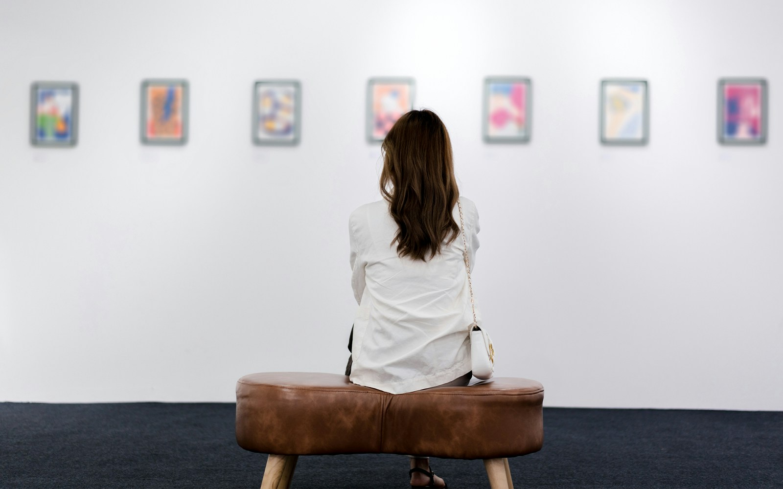 Customer seated in museum viewing abstract paintings on white wall.