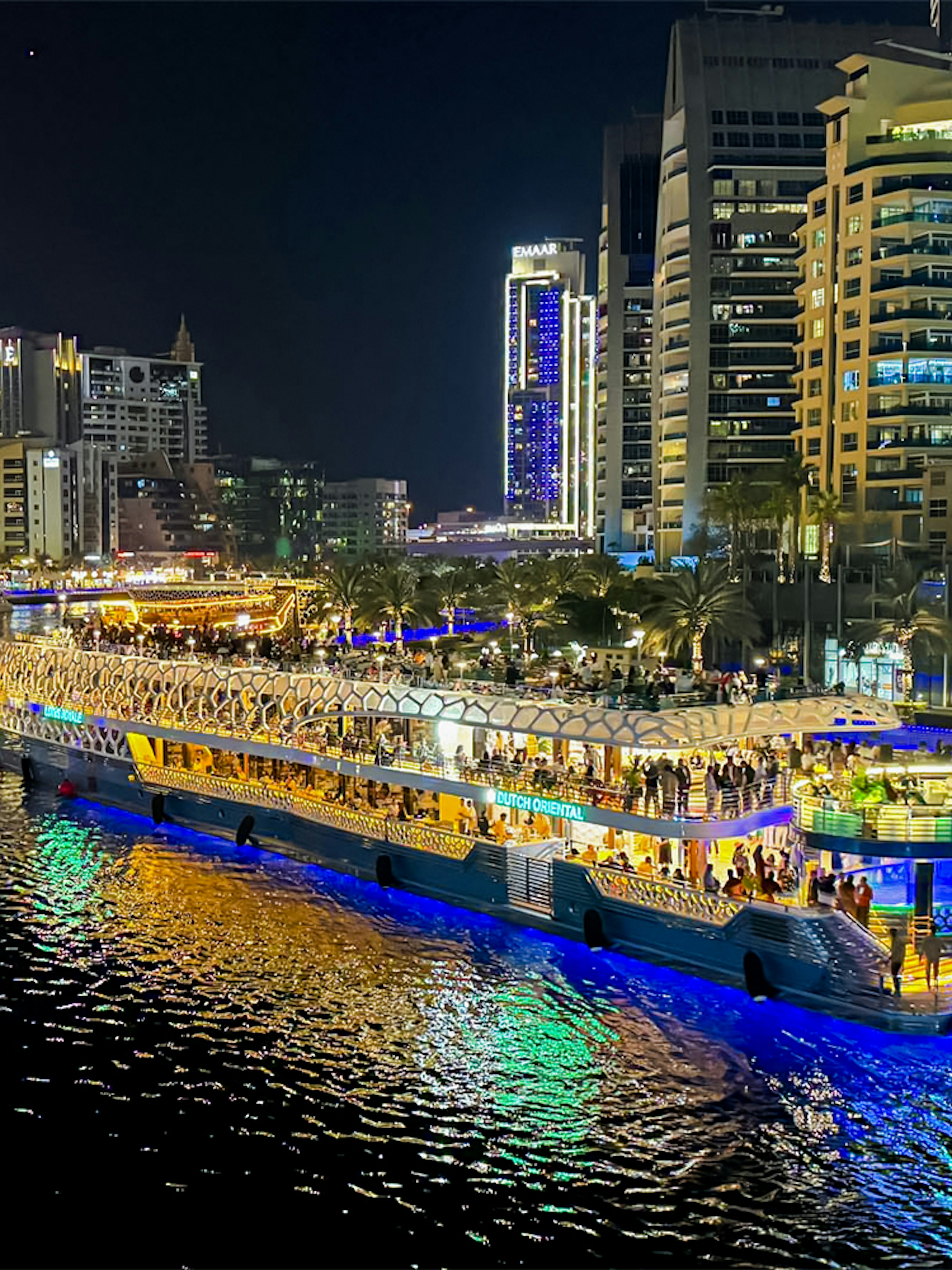 Nighttime cruise on illuminated waterway with city skyline in the background.